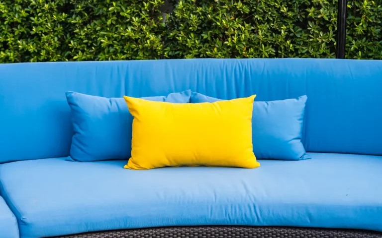 Canapé de jardin bleu avec coussins bleus et un coussin jaune devant une haie verte