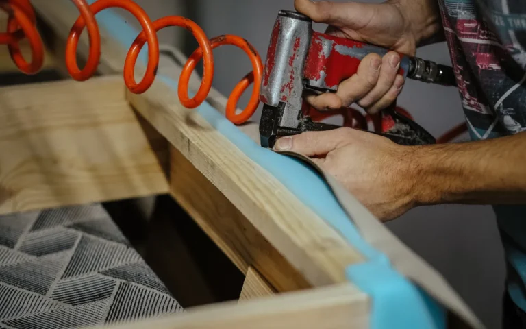 Tapissier fixant un tissu bleu sur un cadre en bois avec une agrafeuse pneumatique