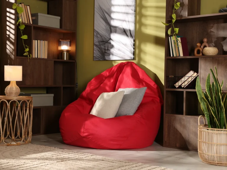 Pouf XXL rouge avec un coussin dans un salon aux murs vert olive, étagères en bois et plantes